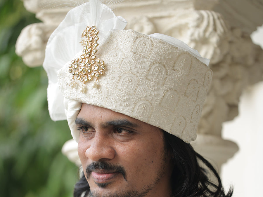 Man wearing a traditional white embroidered outfit with gold details.