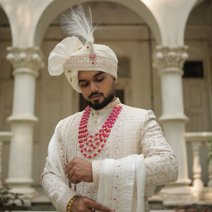 Man in traditional attire with a decorative headpiece in an architectural setting