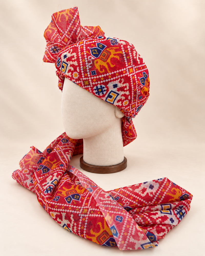 Left side view of red ikat geometric print barati safa showing the smooth wrap and long patterned tail