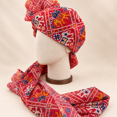 Left side view of red ikat geometric print barati safa showing the smooth wrap and long patterned tail